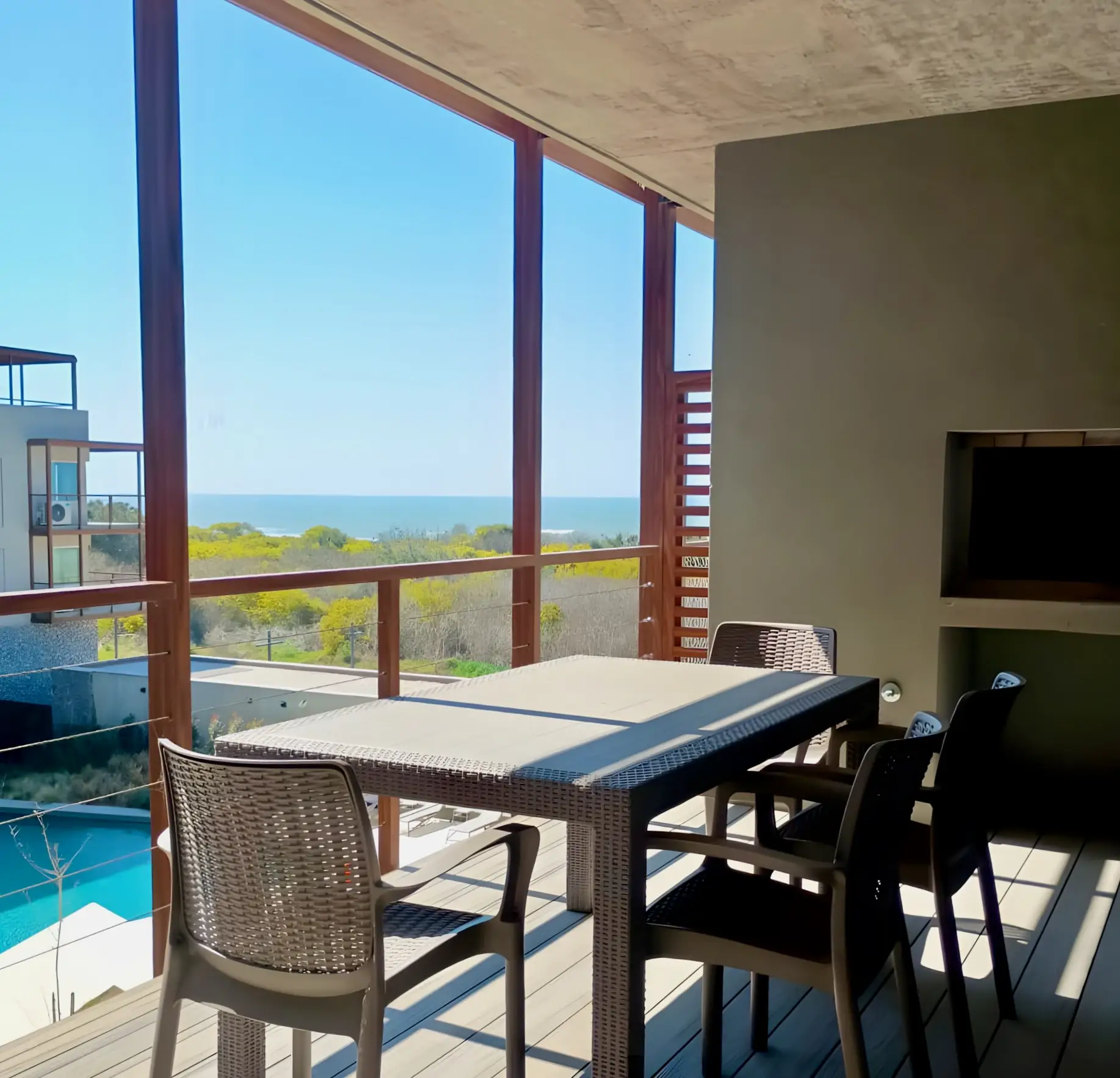 Balcón con mesa para cuatro, parrilla y vista al mar sobre la pileta del complejo