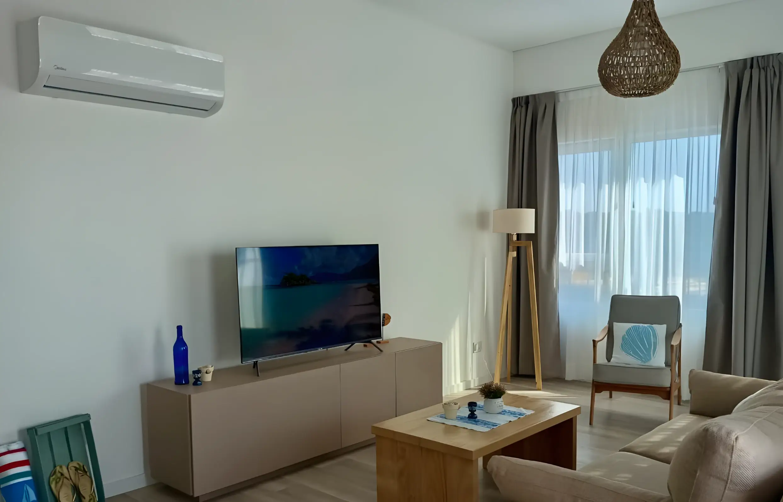Living con televisor, aire acondicionado y sillón junto a la ventana