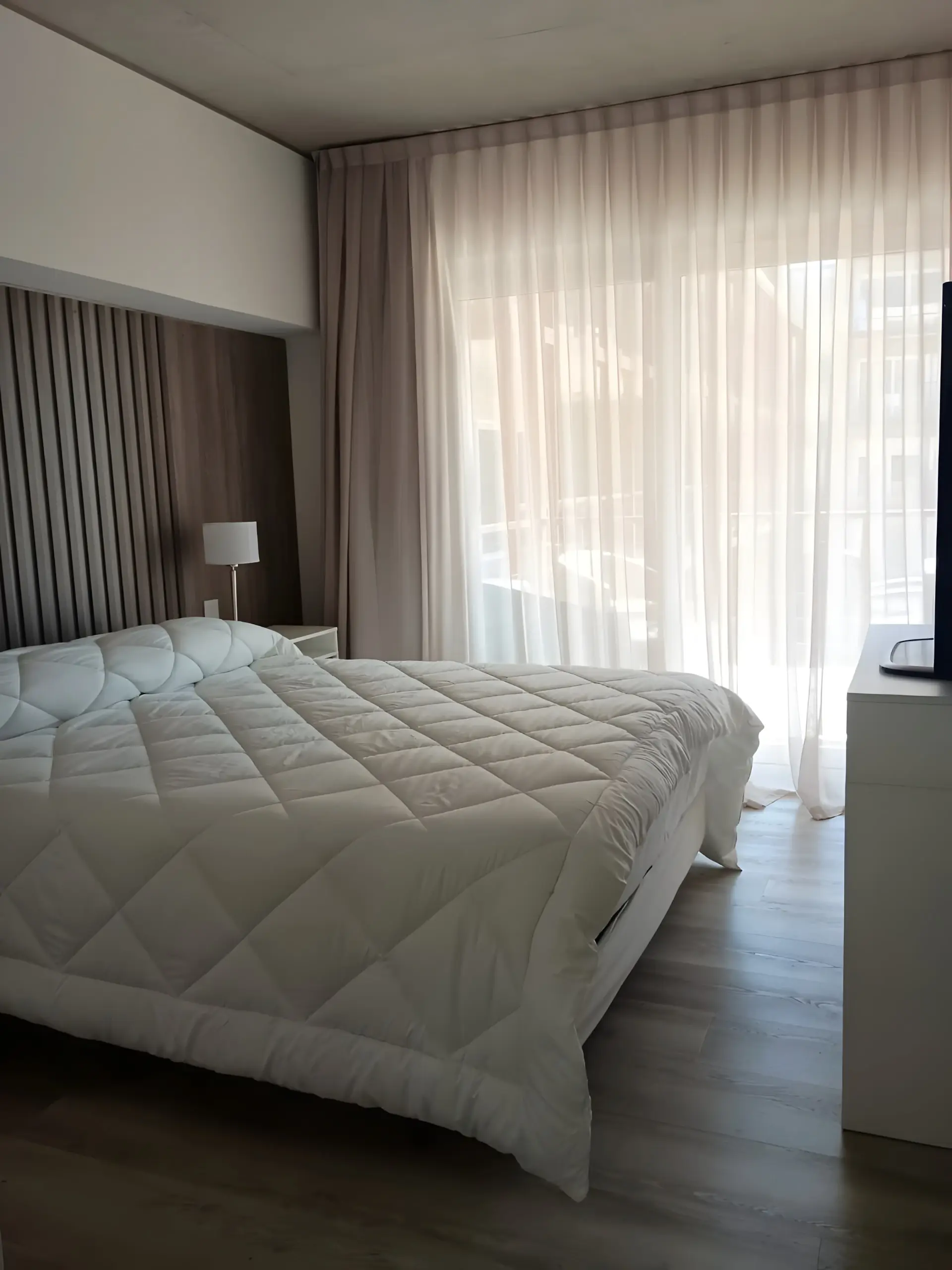 Dormitorio con cama de dos plazas, mesa de luz y salida al balcón